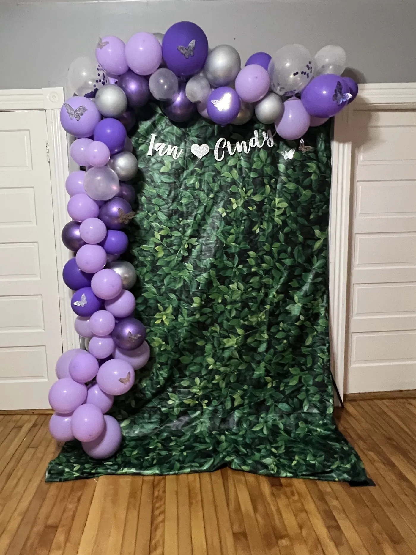 An early setup: a greenery backdrop framed by a purple and silver balloon garland